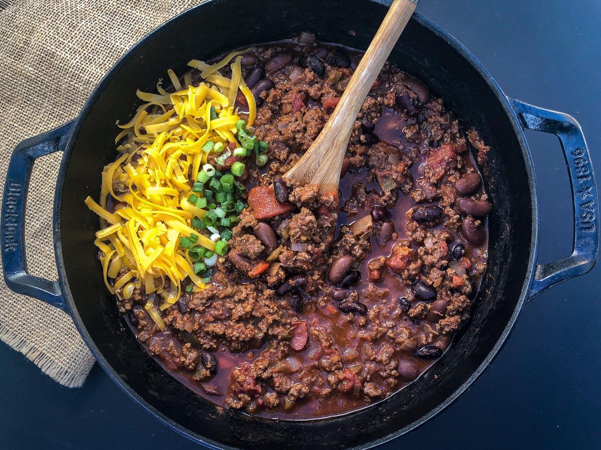 A full pot of awesome chili garnished with shredded cheddar cheese and green onions.