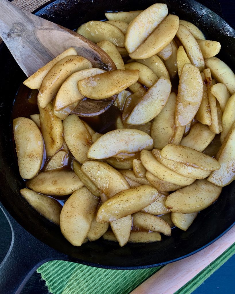 Cast iron skillet of cinnamon apples with a wooden serving spoon.