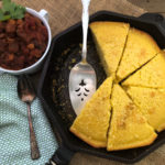 Sliced sweet cornbread in a skillet with a cup of chili.