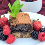 Chocolate chip cookie brownie on a white plate with a trio of berries.