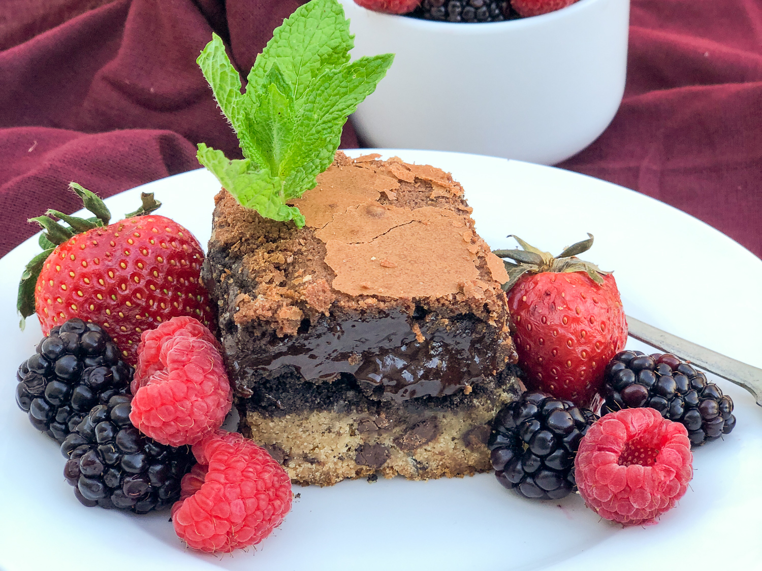 Chocolate chip cookie brownie on a white plate with a trio of berries.