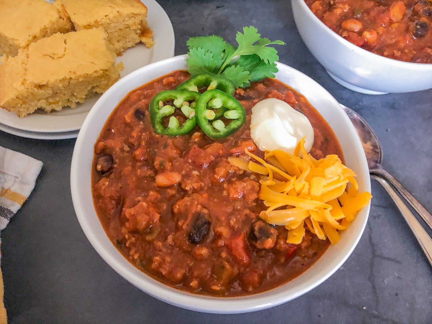 Pumpkin chili in a white bowl garnished with cilantro, sour cream, jalapeños, and cheese.