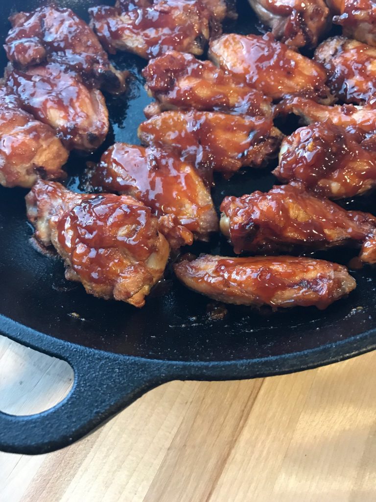 Off center view of sticky chicken wings in a cast iron pan. 