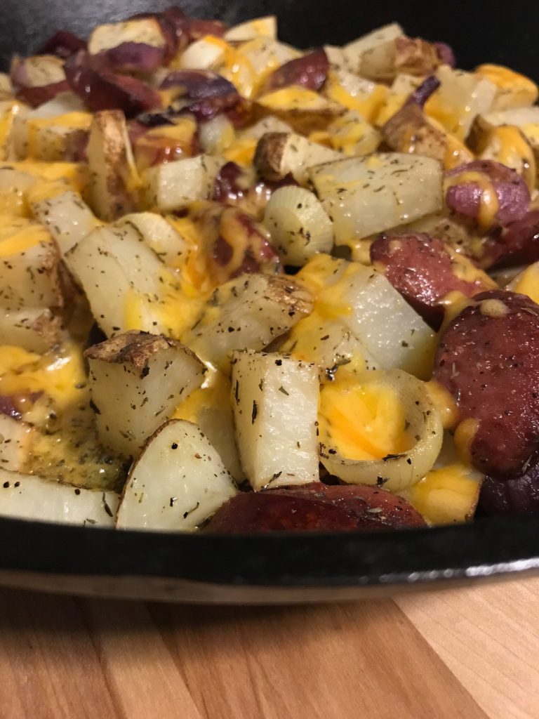 Skillet full of cheese, sausage, onions, and potatoes. 