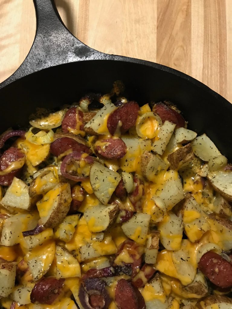 Cast iron skillet of sliced sausage, potatoes, onions, and cheese