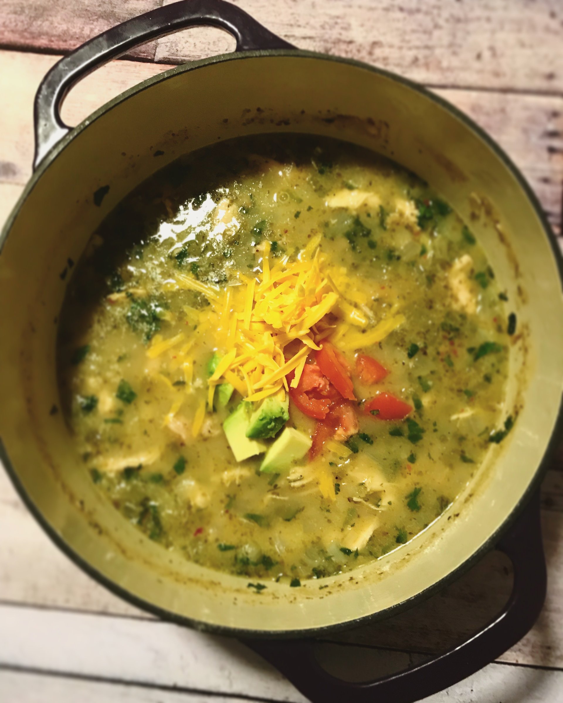 Top view of white chicken chili in the dutch oven topped with cheese, tomatoes, and avocado.