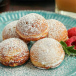 5 Danish aebelskiver on a blue plate with raspberries.