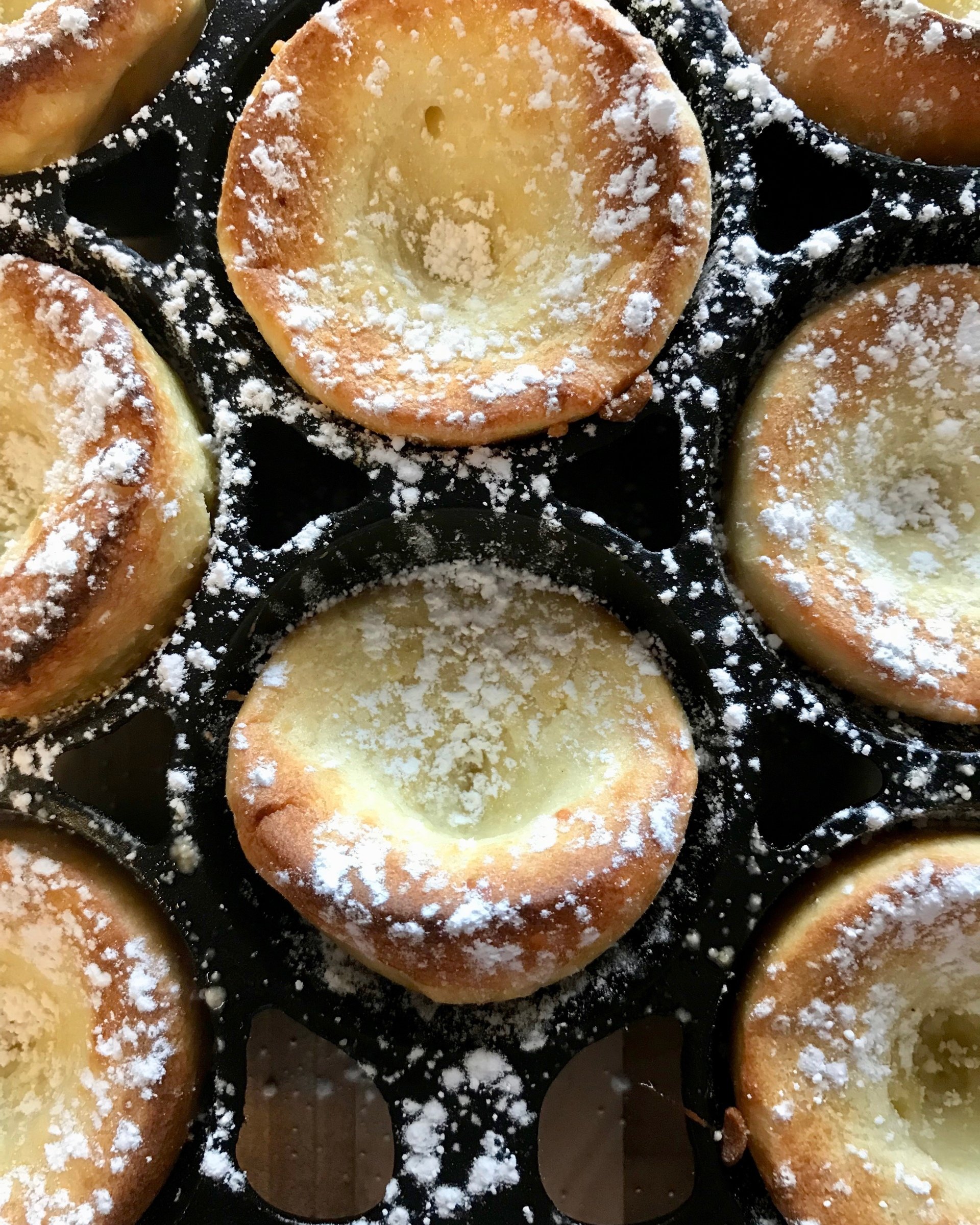 Popovers in cast iron bakeware sprinkled with powdered sugar.