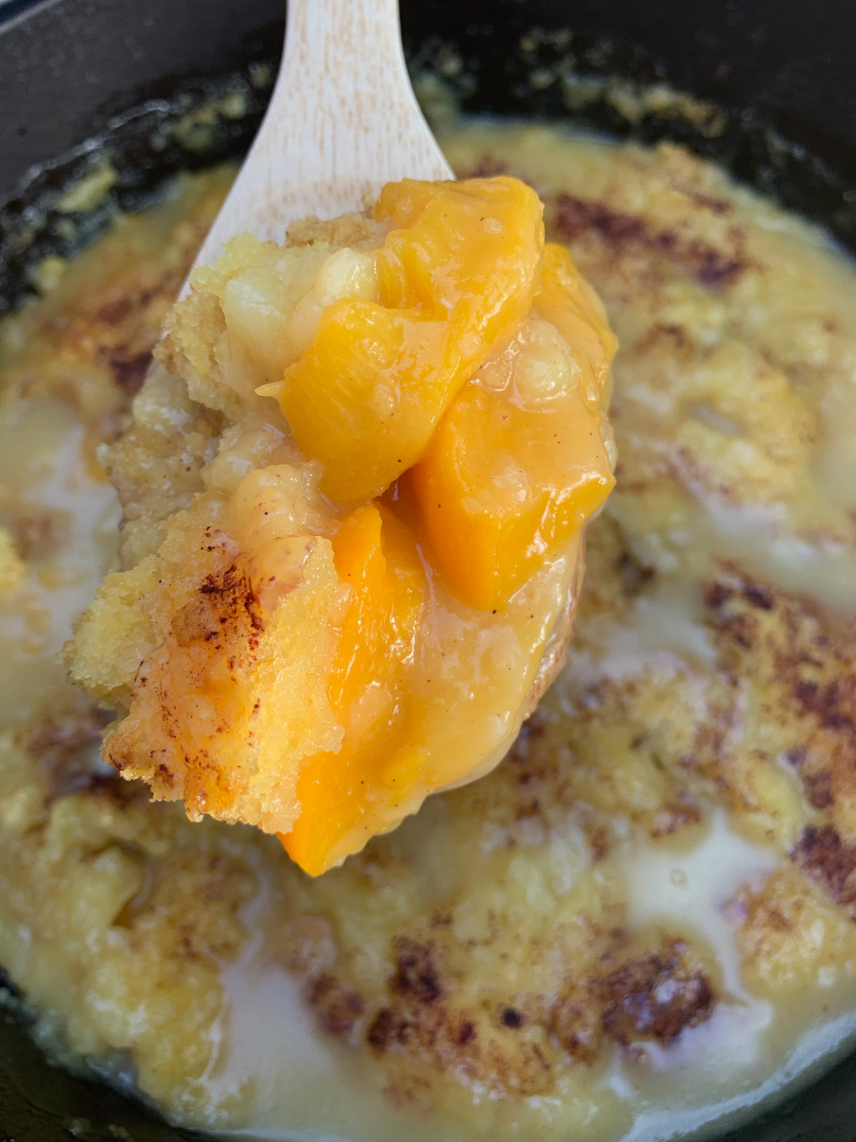 Peach dump cake with a wooden spoon lifting up a serving. 