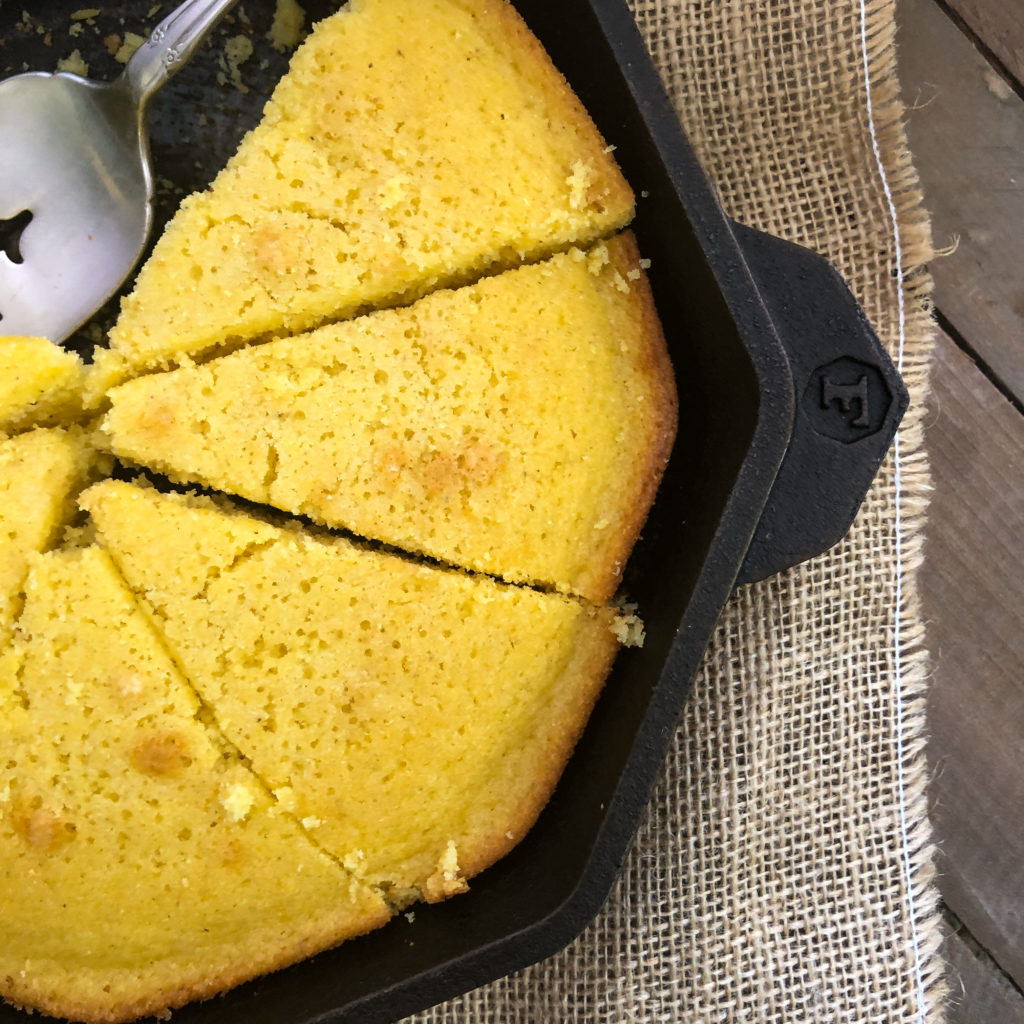 Close up view of sliced sweet cornbread in the cast iron skillet with a serving utensil. 