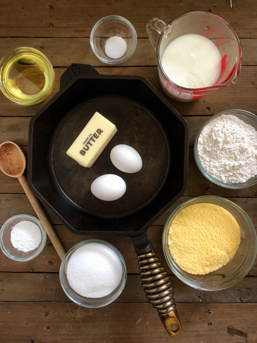 Each ingredient needed to make this cornbread recipe in individual bowl or in the cast iron skillet.