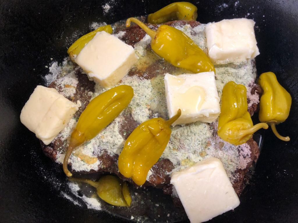 Cubed butter, peperoncini peppers with ¼ cup of their liquid have been added to the roast in the Dutch oven.