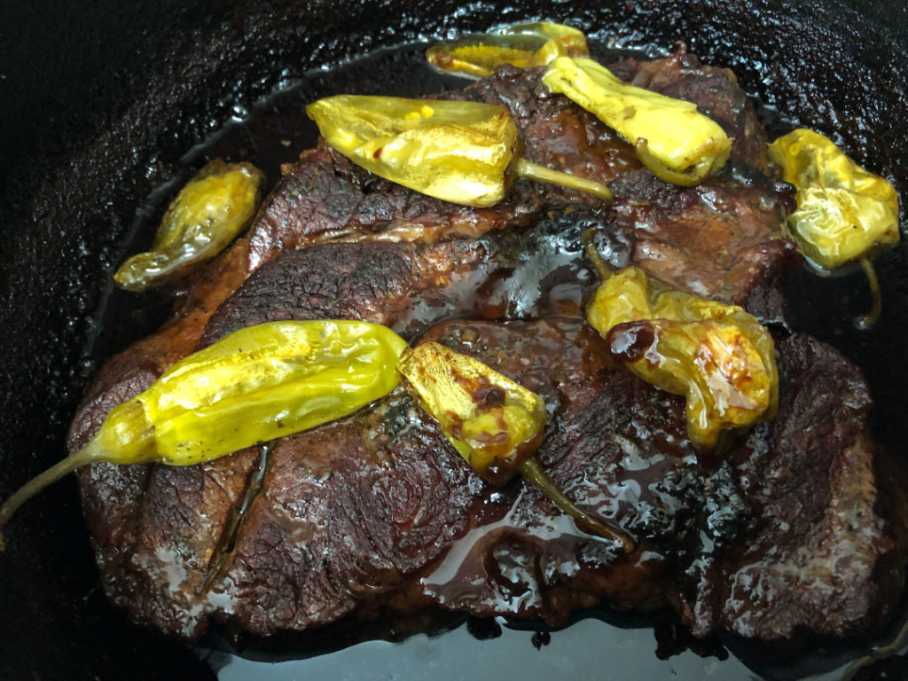 Mississippi Pot Roast cooked in a Dutch oven with peperoncinis on top. 