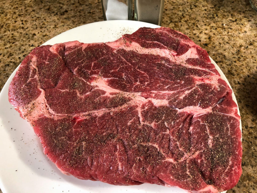 Chuck roast liberally seasoned with salt and pepper on a plate before searing.