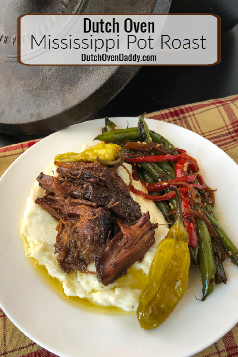 Plated pot roast over mashed potatoes with a side of green beans. Dutch oven in the back ground. 