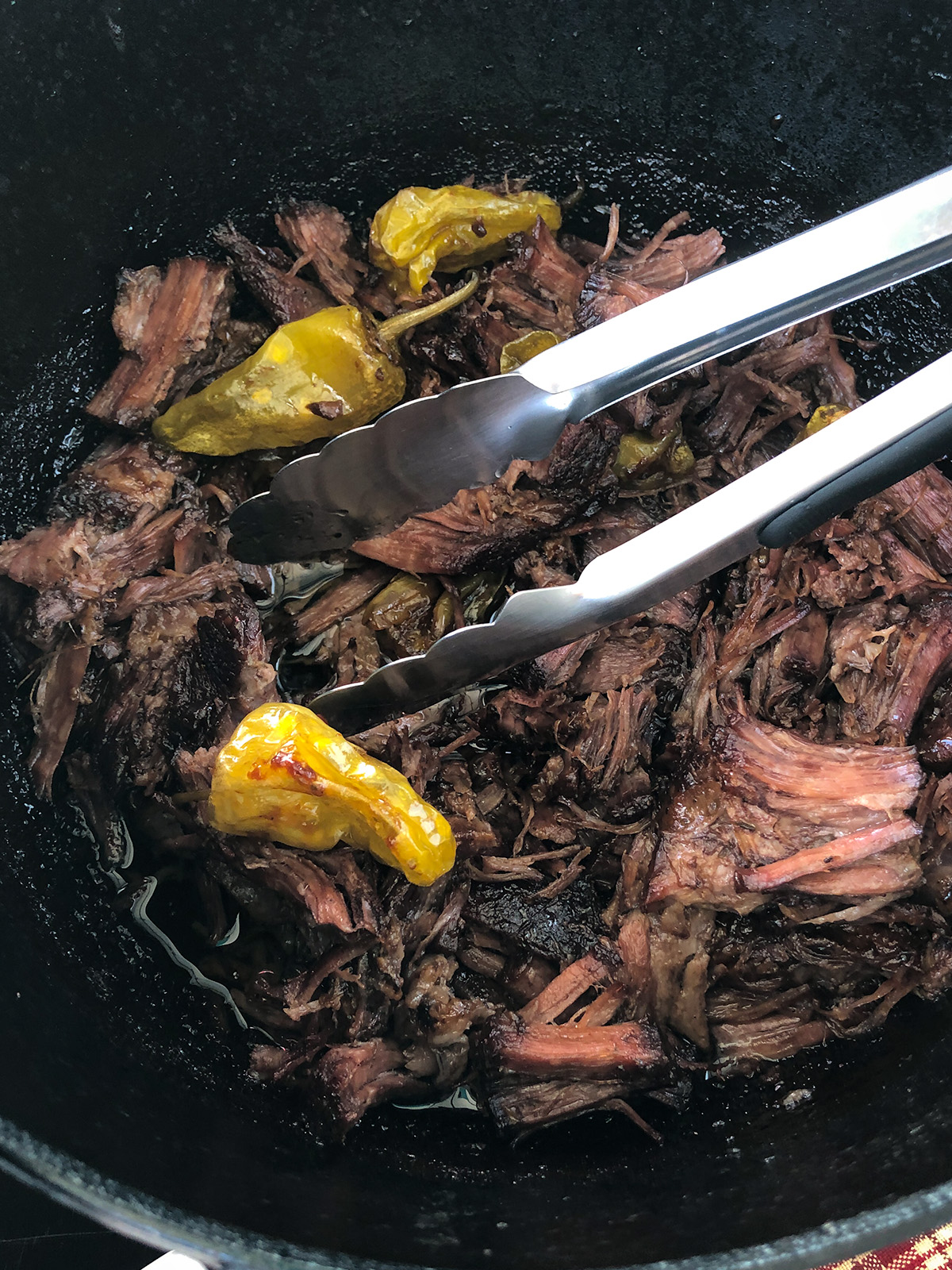 Tongs grabbing shredded Mississippi pot roast from a Dutch oven.
