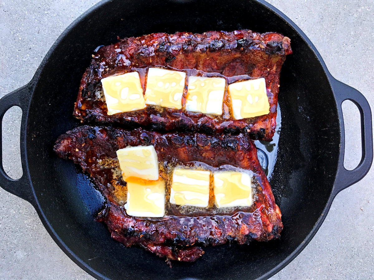 Cooked ribs in a Dutch oven with butter pats and drizzled with honey. 