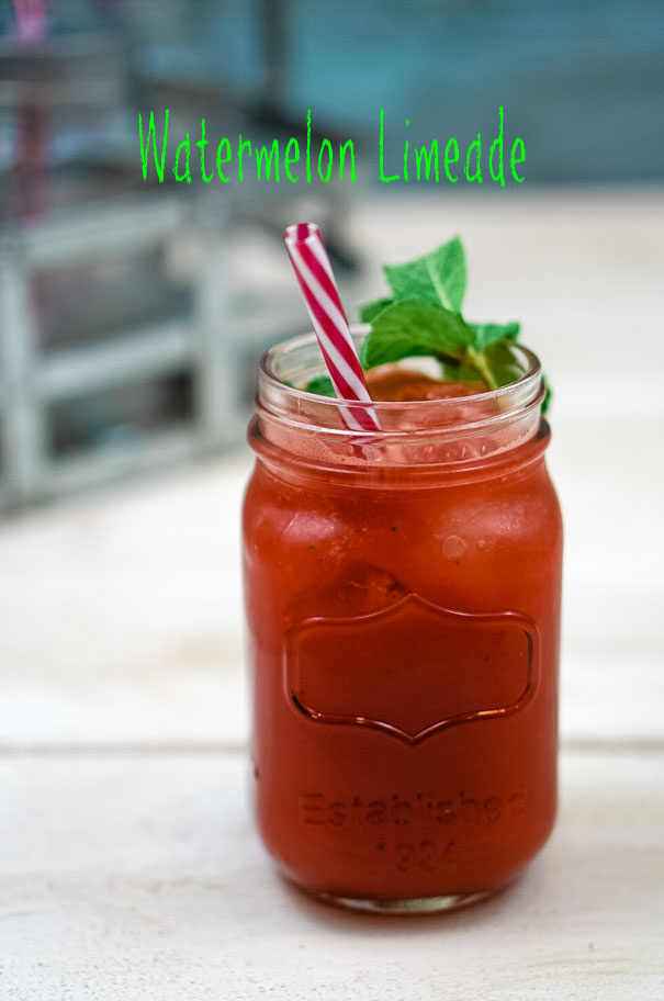 Fresh watermelon limeade in a mason jar glass with a red and white straw and garnish of fresh mint. 