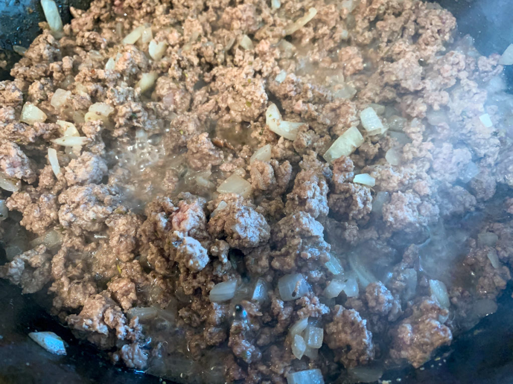 Ground beef being cooked in the dutch oven with onions and seasonings. 