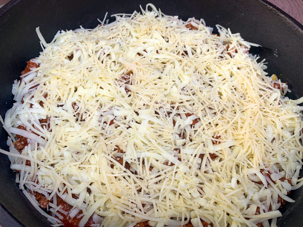 Pramesan and mozzarella cheeses have been added to the top layer of the now contructed lasagna. 