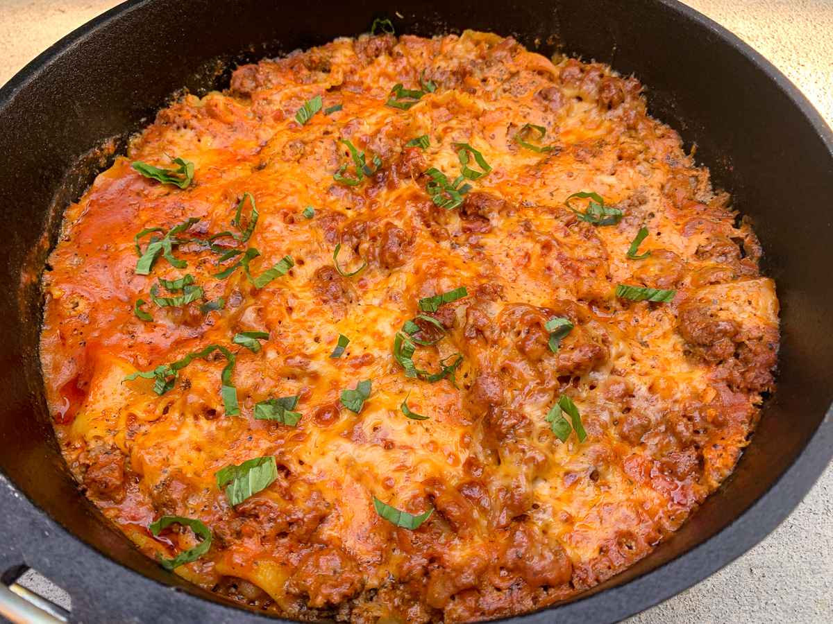 The camp oven lasagna has cooked, rested, and been garnished with fresh basil and is ready to serve.