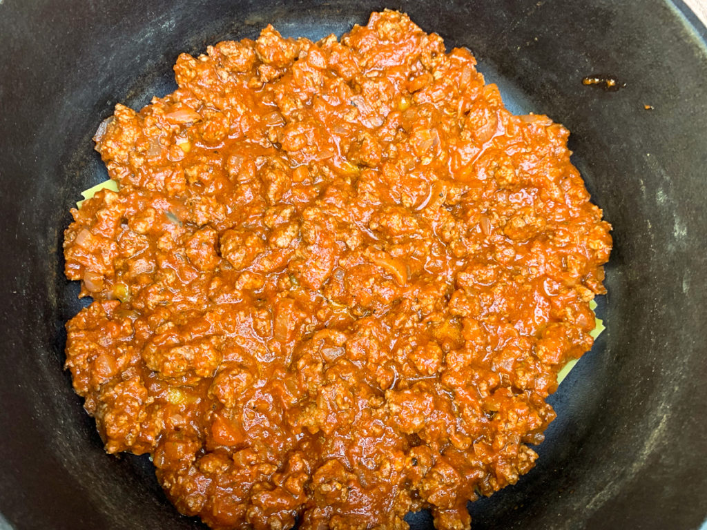 The meat sauce has been spooned evenly over the bottom or first layer of lasagna noodles.