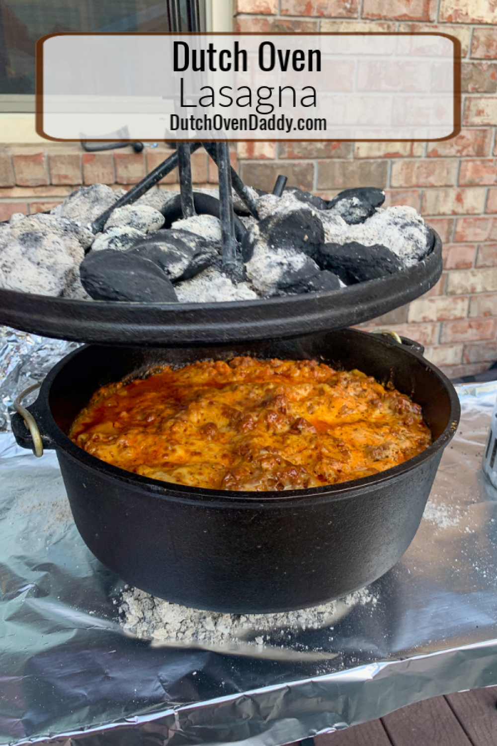 The lid being raised off the camp oven with the charcoal on top revealing the cooked lasagna.