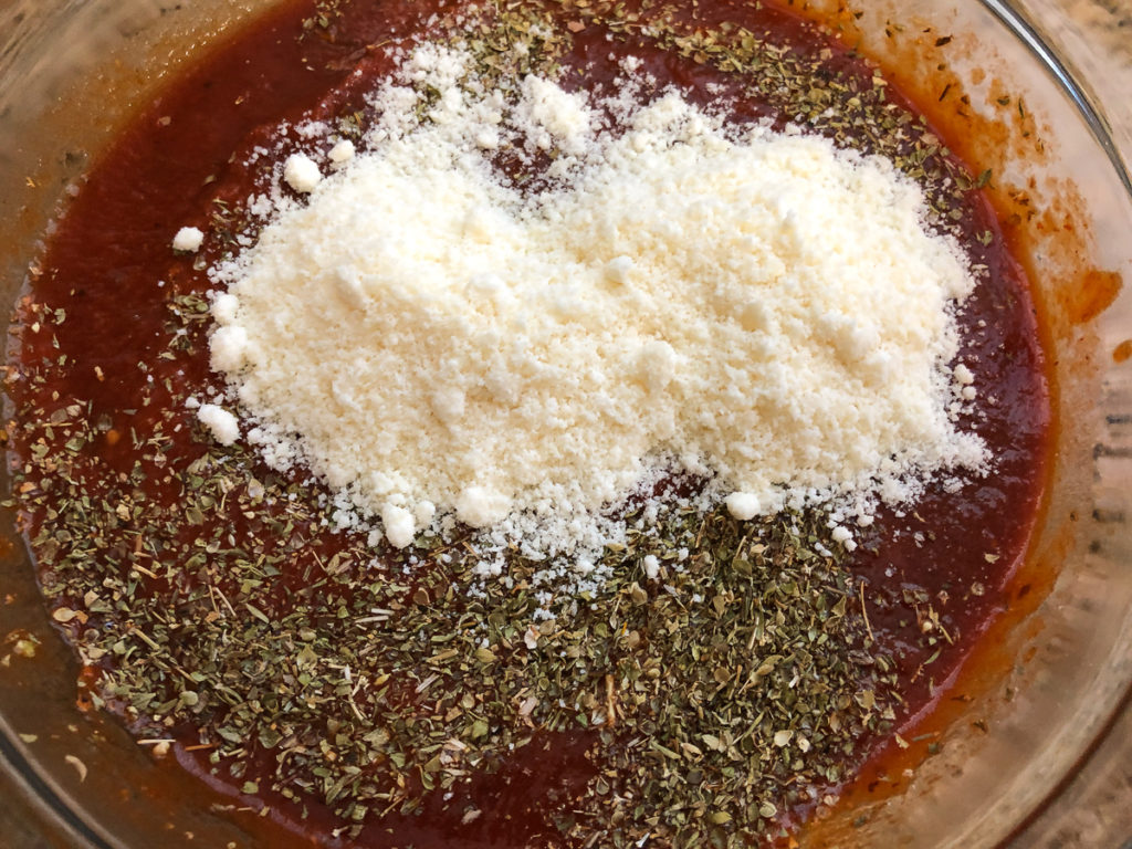 The jarred pizza sauce has been added to a bowl with oregano and some parmesan cheese.