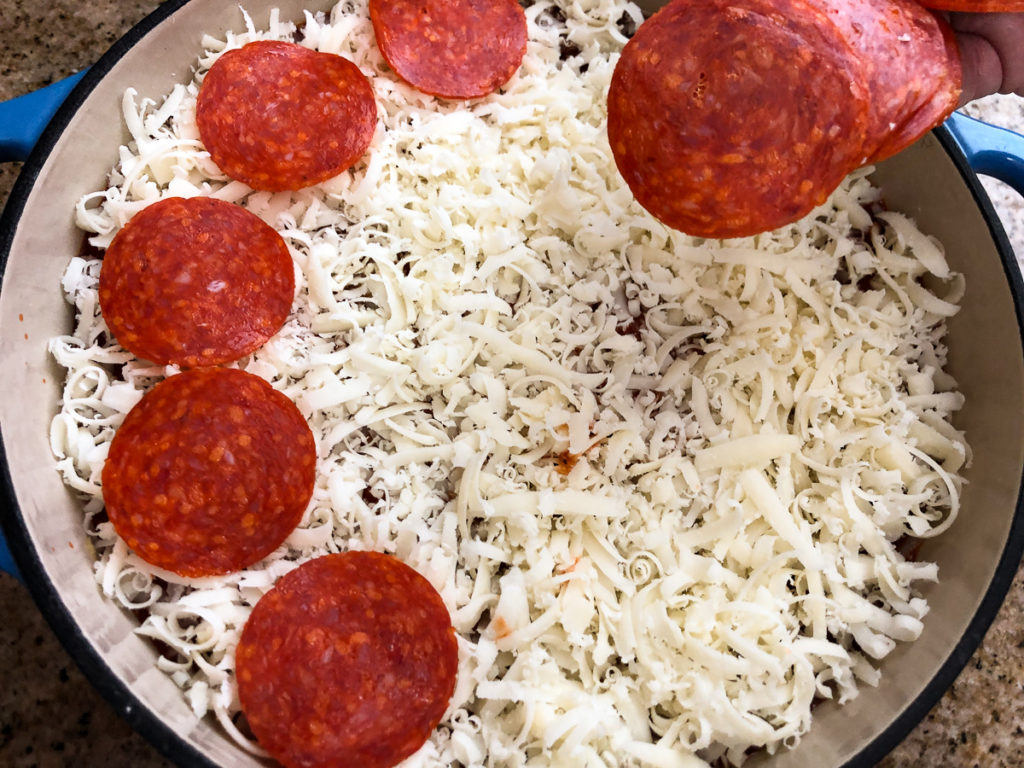 Sliced pepperoni is being added to on top of the shredded mozzarella. 