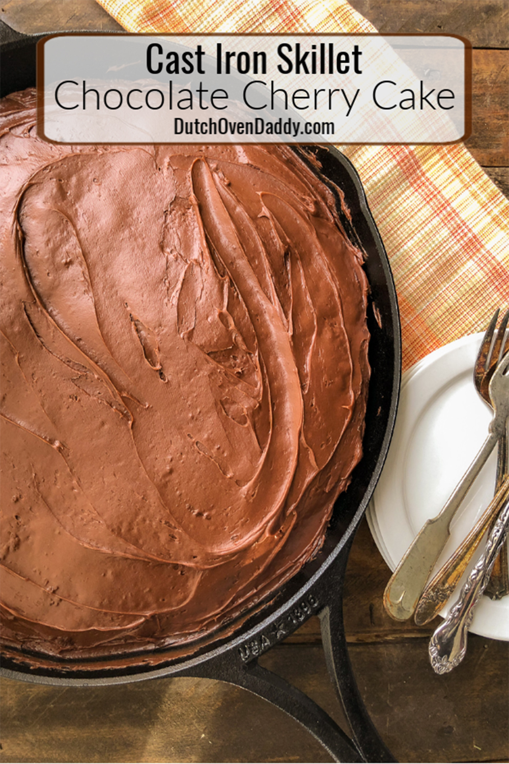 Close up view of the frosted and ready to be served chocolate cherry pie in the skillet with forks and plates off to the side. 