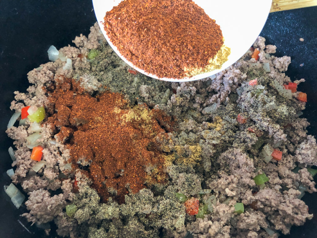 Seasonings being added to the browned beef, onions, and bell peppers in the dutch oven.