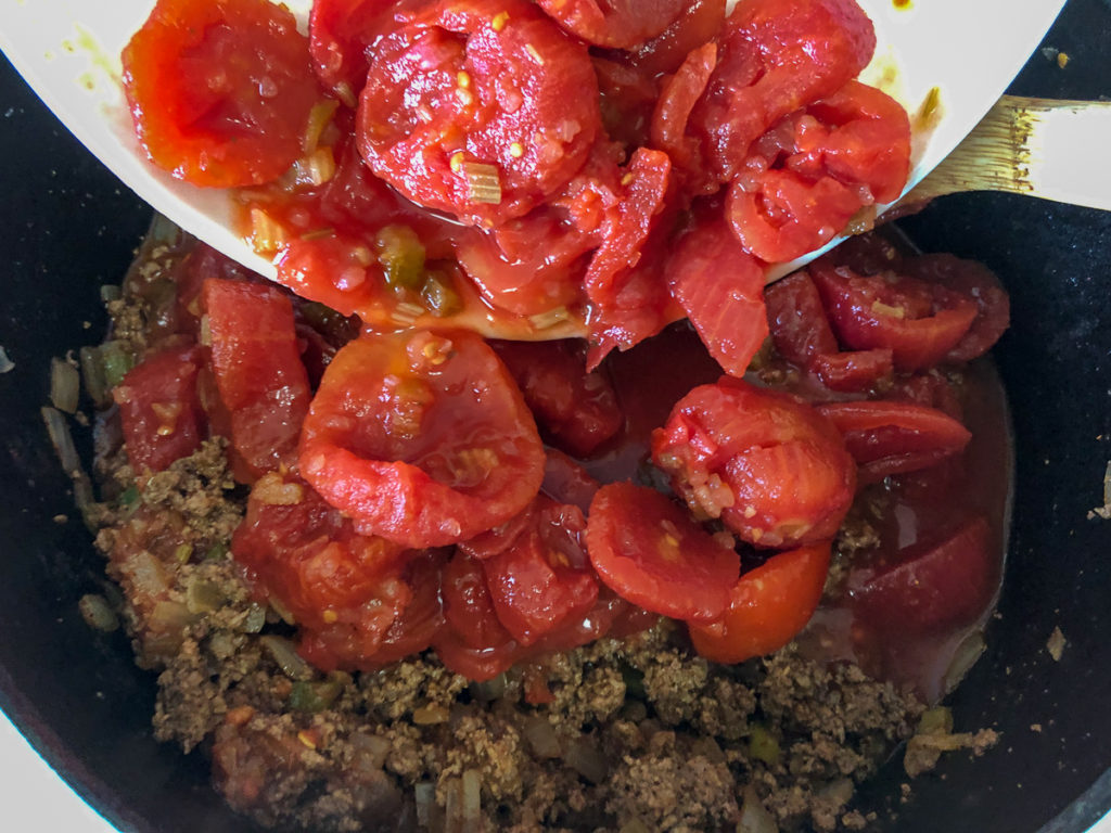 The salsa and tomatoes are being added to the chili base in the dutch oven.