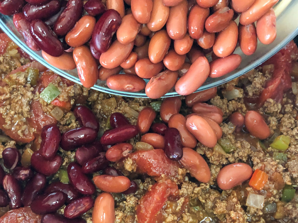 The dark and light kidney beans are being added to the chili in the dutch oven. 