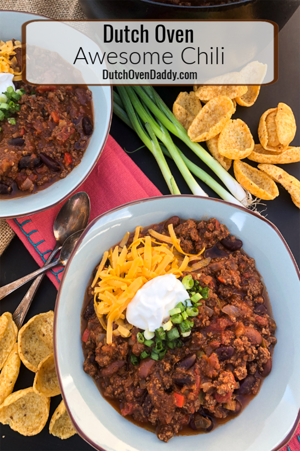 Awesome Chili served up in bowls topped with sour cream, cheddar cheese, and green onions, Frito chips sprinkled around. 