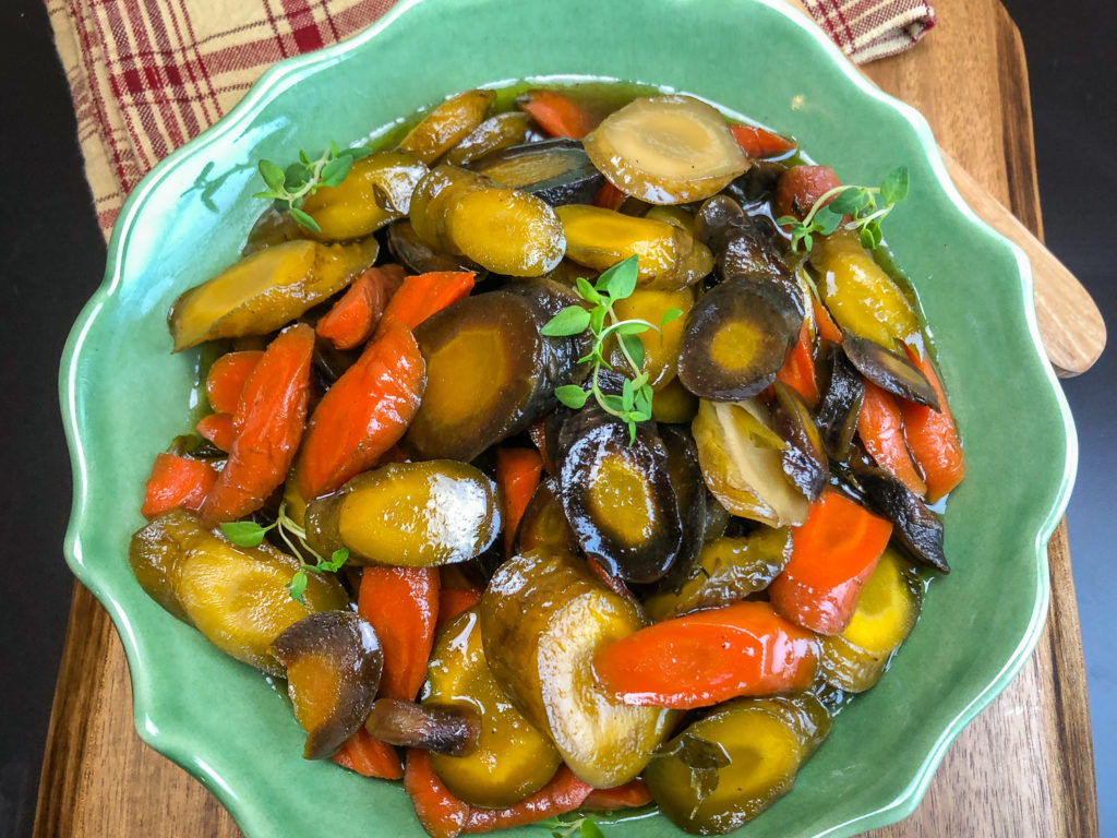 Dutch oven honey glazed carrots in a green serving bowl garnished with fresh thyme. 