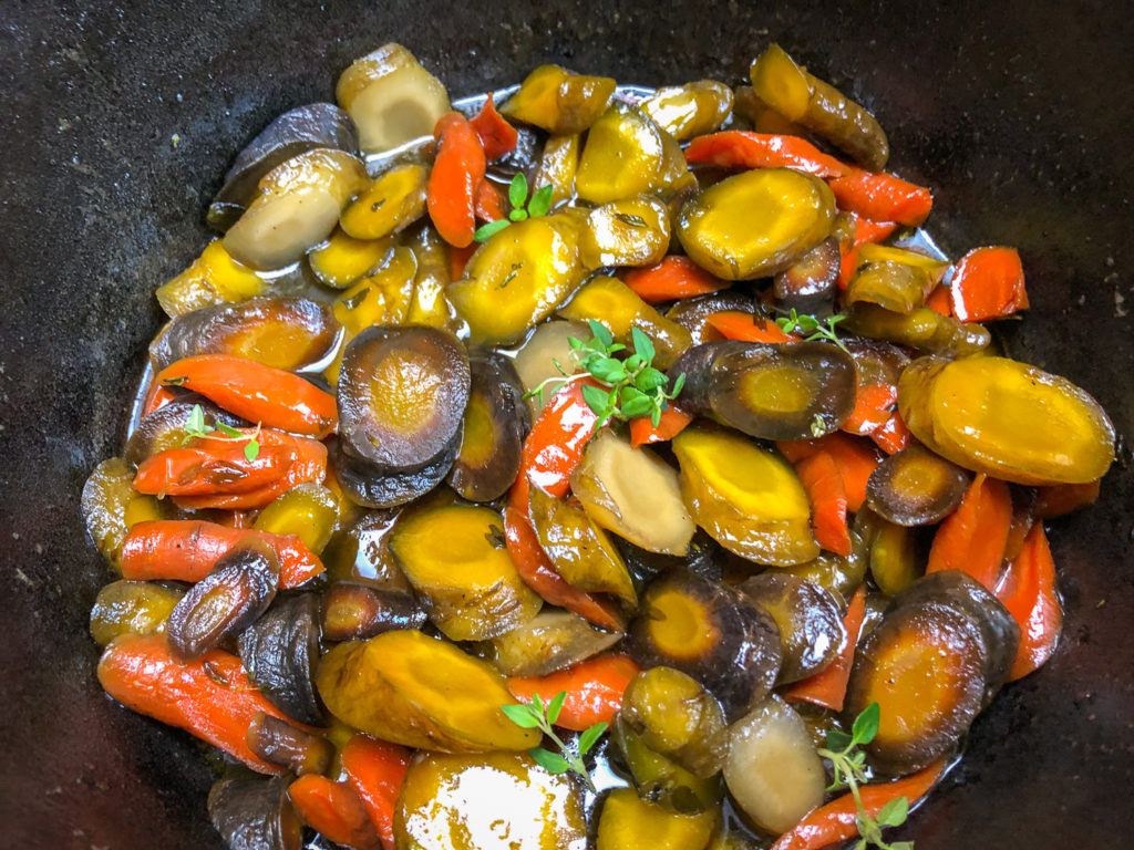 Cooked rainbow carrots garnished with fresh thyme in a honey glaze sauce that has been reduced. 