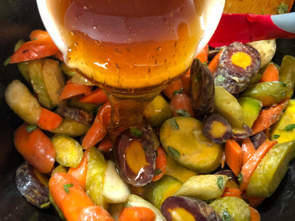 Honey being poured over the seasoned carrots in the Dutch oven.