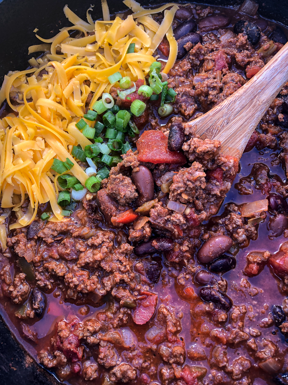 Dutch oven chili with a wooden spoon scooping up a bit. 