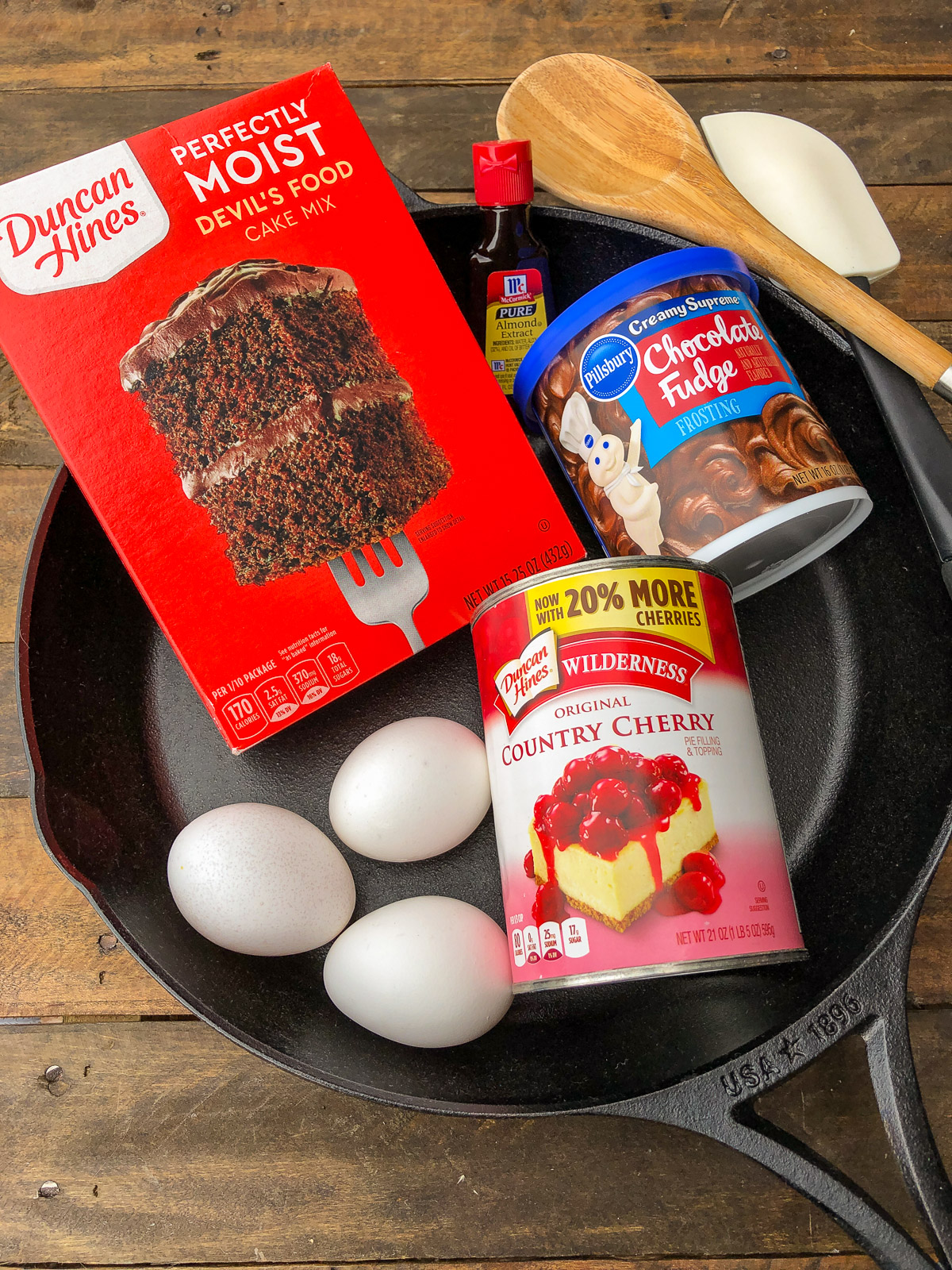 Cherry chocolate cake ingredients (devil's food cake mix, cherry pie filling, eggs, and almond extract) in a cast iron skillet.