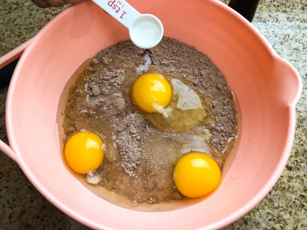 Cake mix, three eggs, and almond extract added to a pink mixing bowl. 