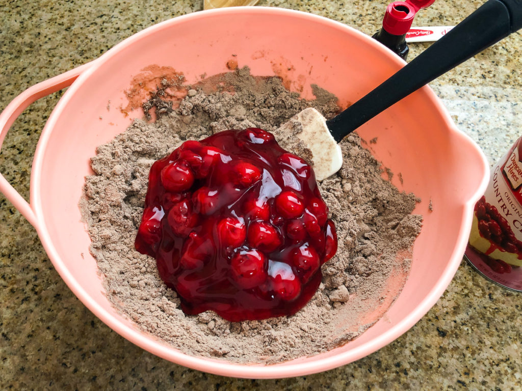 Half of the cherry pie filling can has been added to the mostly dry cake mix. 
