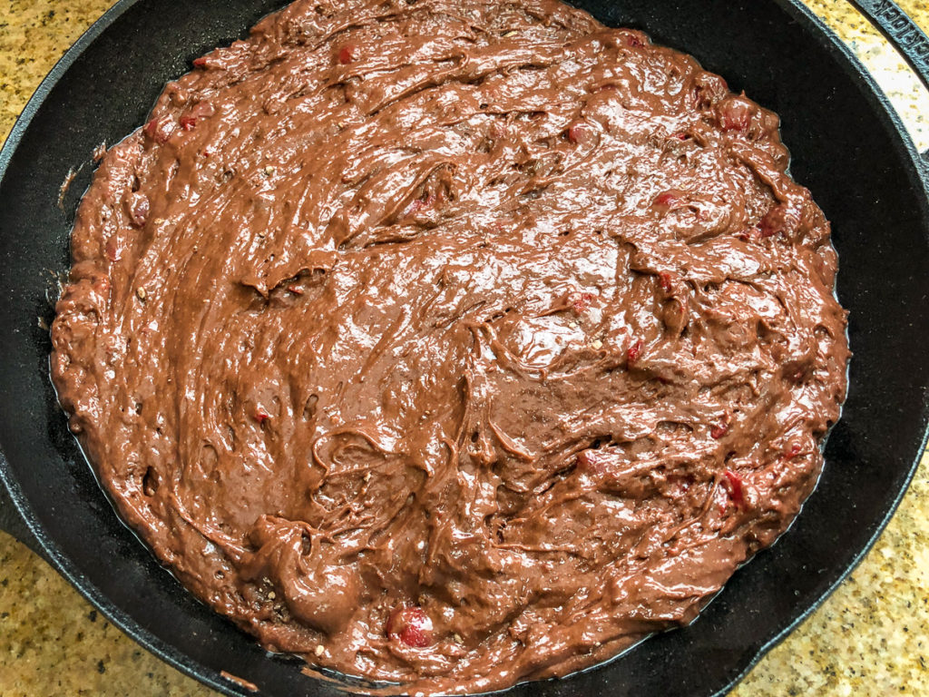 Chocolate cherry cake batter has been poured and smoothed into the prepared cast iron skillet. 