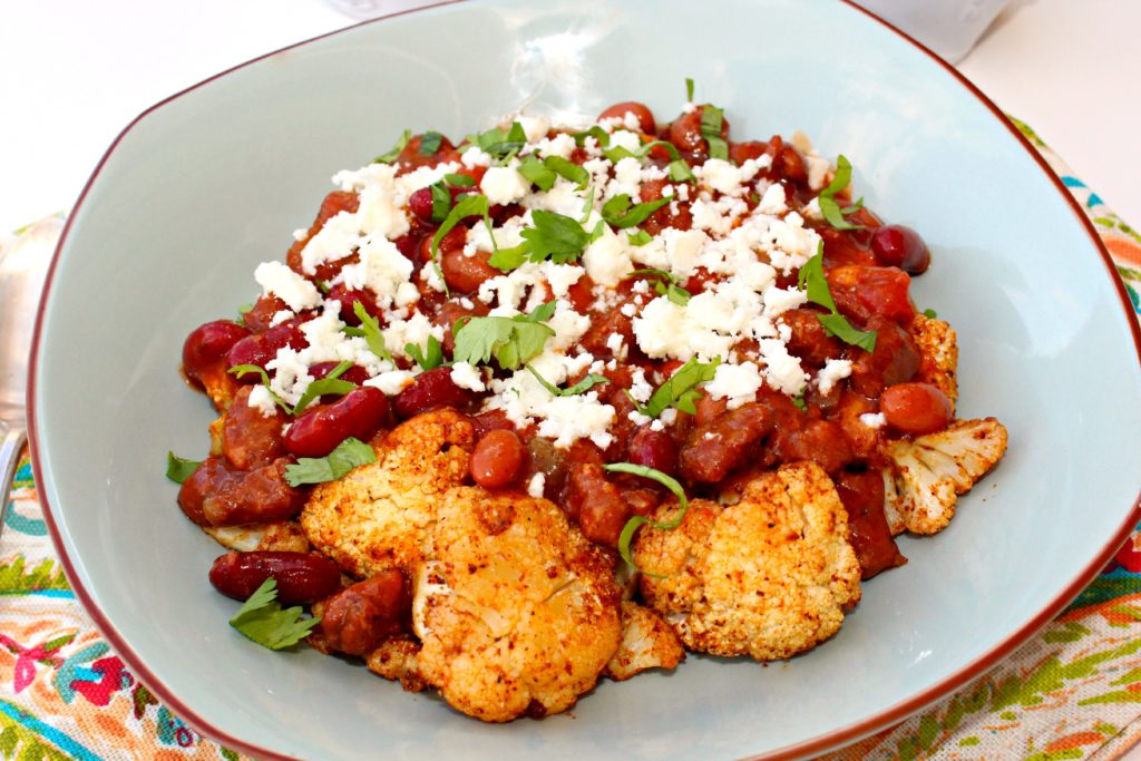 A bowl of roasted spiced cauliflower topped with chili, queso fresco, and cilantro. 