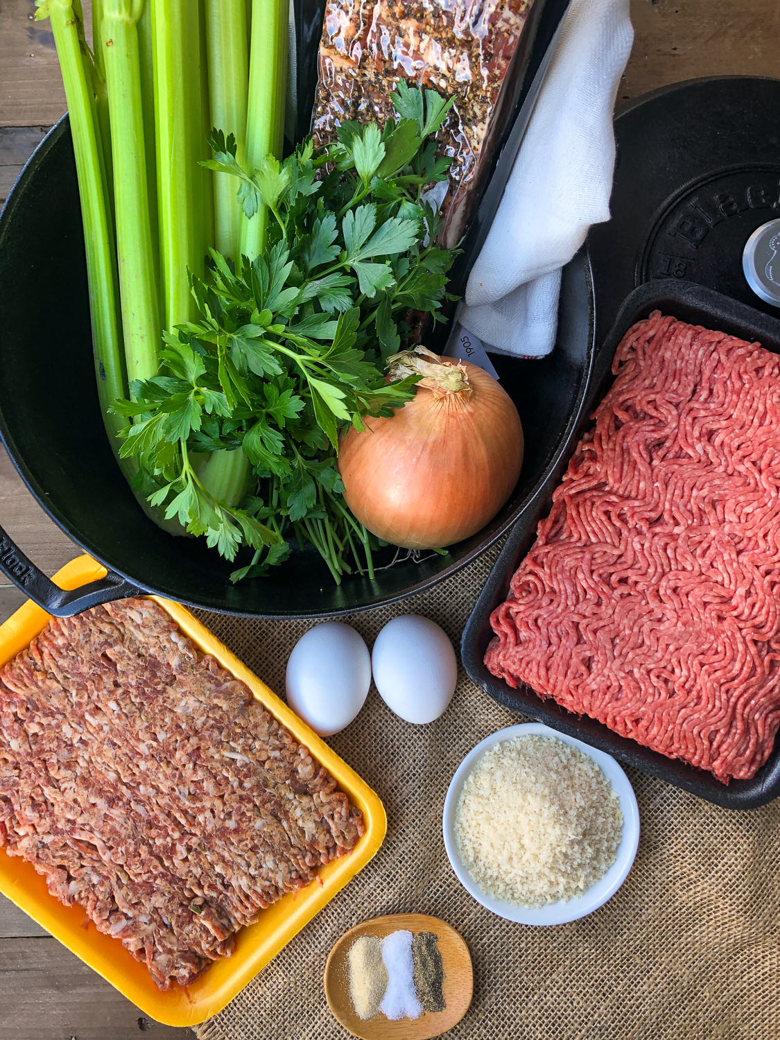 Ingredients to make the meatloaf: ground Italian sausage, ground beef, eggs, panko, onion, celery, peppered bacon, fresh parsley, seasonings, and a dutch oven.