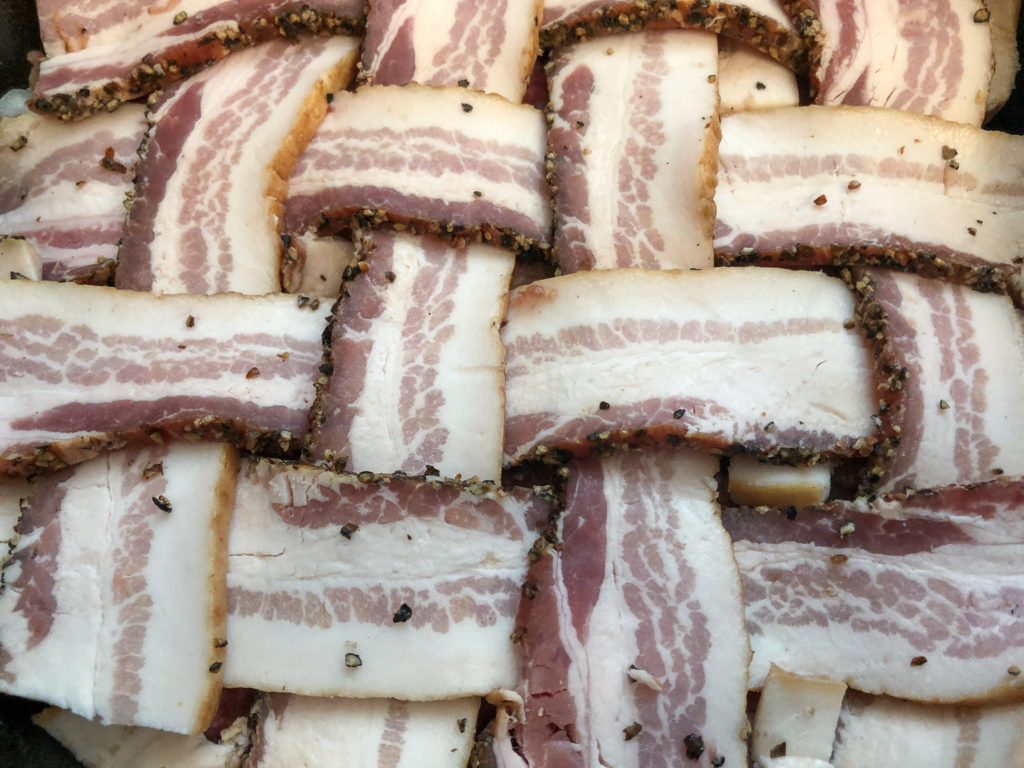 Peppered bacon has been applied to the top of the meatloaf in a lattice weave. 