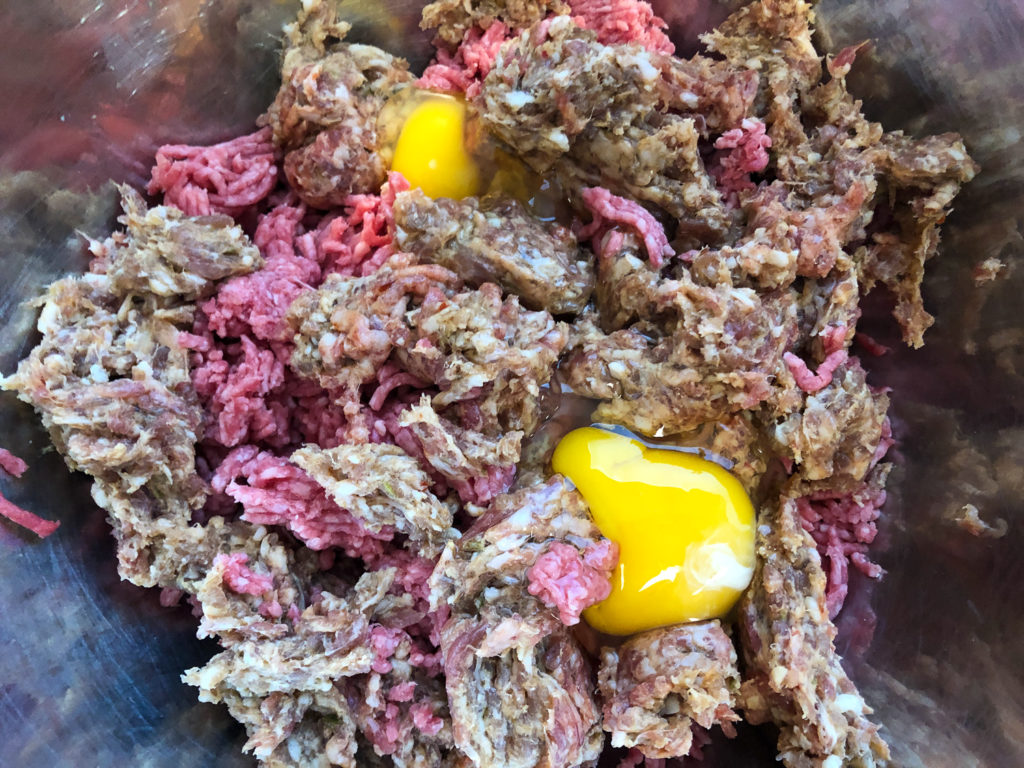 Two eggs have been added to the crumbled meats in the large bowl. 