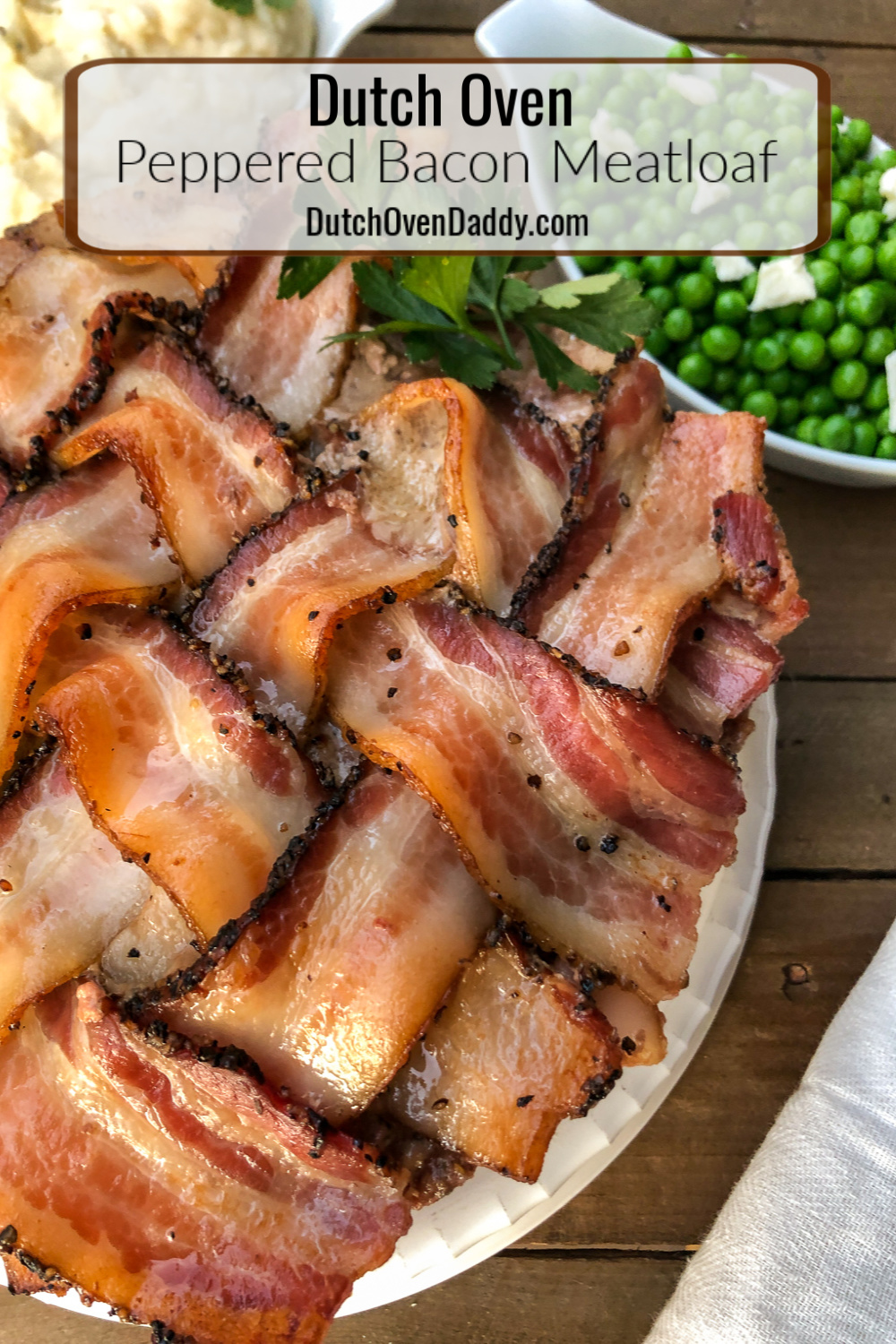 Mashed potatoes and peas in the background with peppered bacon meatloaf plated in the center. 