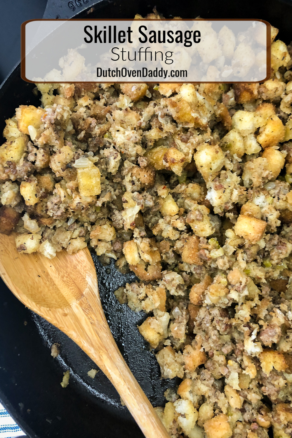 Cast iron skillet full of sausage stuffing with a portion removed and a wooden spoon.