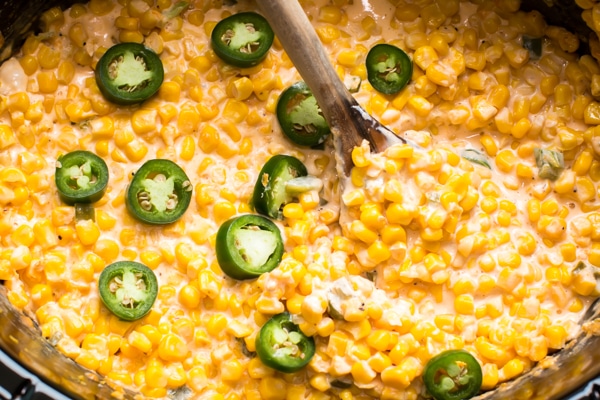 Slow cooker crock full of cheesy creamy corn with slices for fresh jalapeño. 