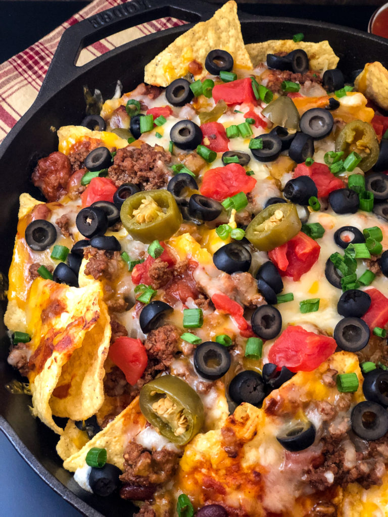 Side view of skillet nachos loaded with toppings. 